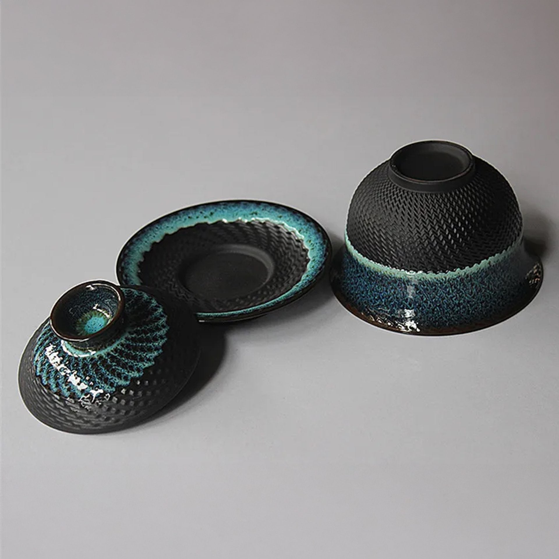 Blue textured tea set with bowl, lid, and saucer on grey.