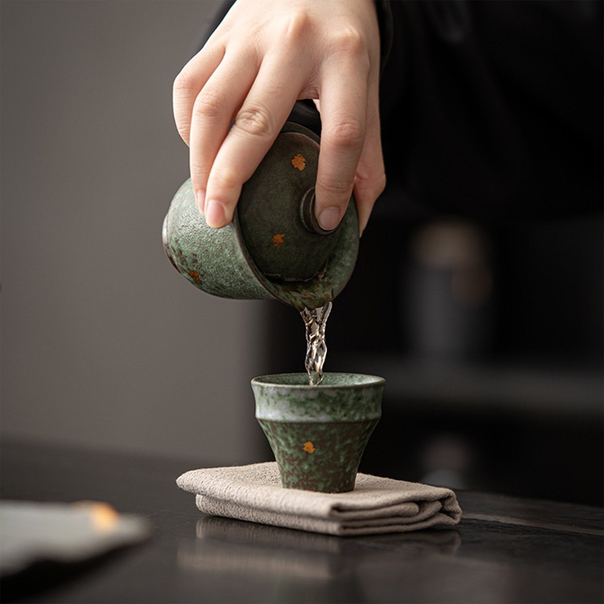 Pouring water from green teapot into cup on a fabric-covered tray