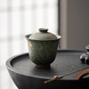 Green teapot with gold accents on black circular tray, soft focus background