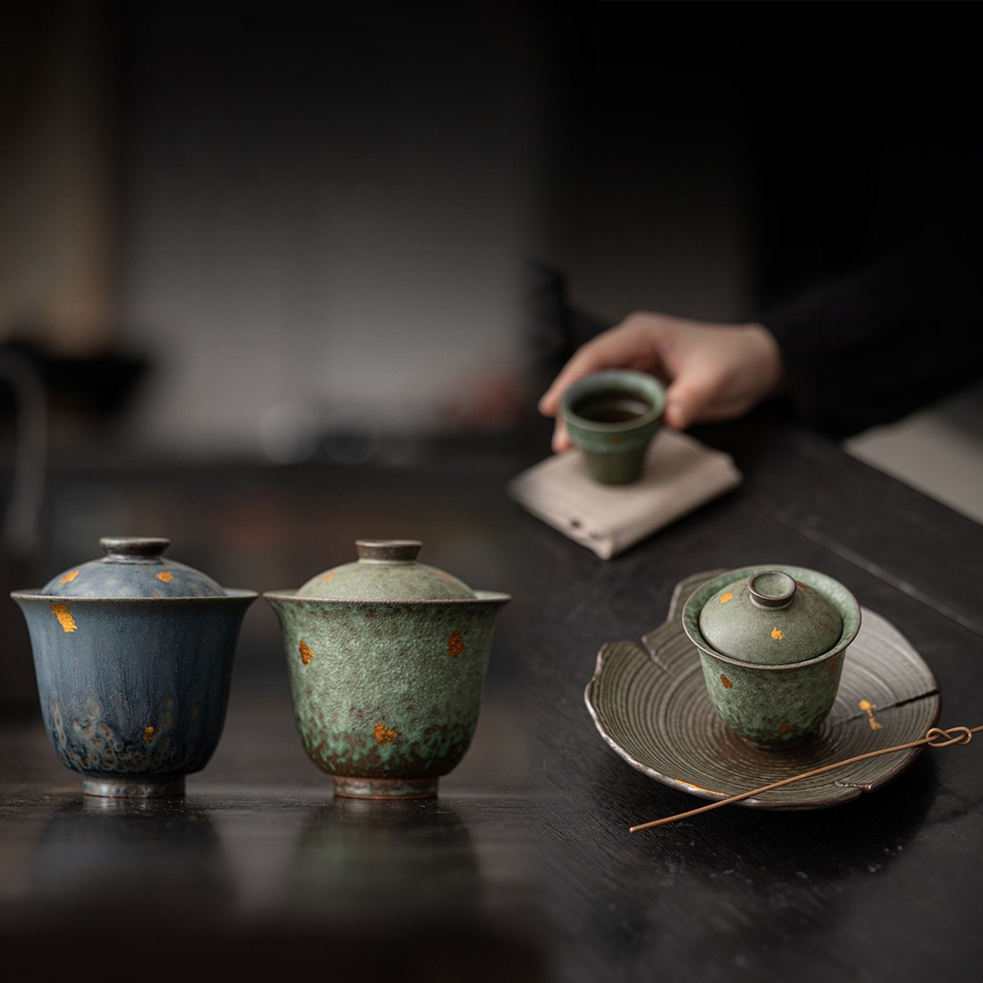 Vintage teapots and cup on a dark wooden table with a hand in view