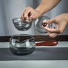 Transparent glass teapot with detachable lid and wooden handle.