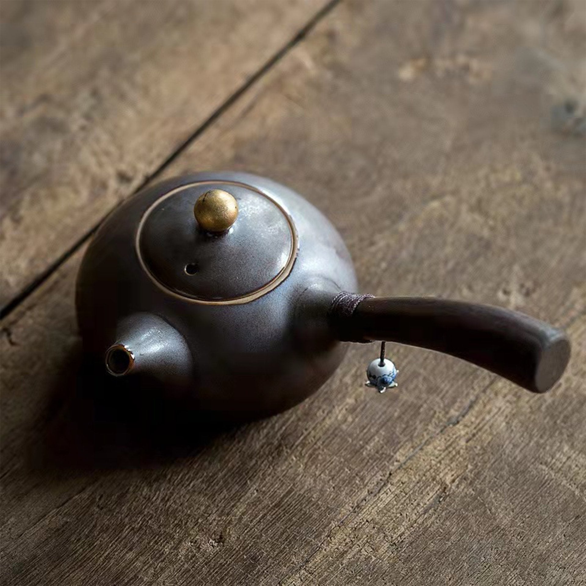 Side-handle teapot with a black body and wooden handle on a wooden surface