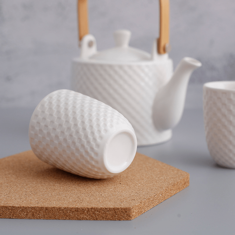 Angle view of a teapot and cup emphasizing the textured white ceramic and modern aesthetic.