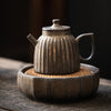 Vintage textured stoneware teapot on a woven mat in a rustic tray.