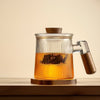 Glass tea infuser mug filled with amber-colored tea on a wooden stand, showcasing its design and clarity.