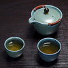 Green teapot with tea cups filled with tea on dark wooden background