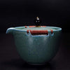 Green ceramic teapot with brown rope handle and black bead on top against dark background