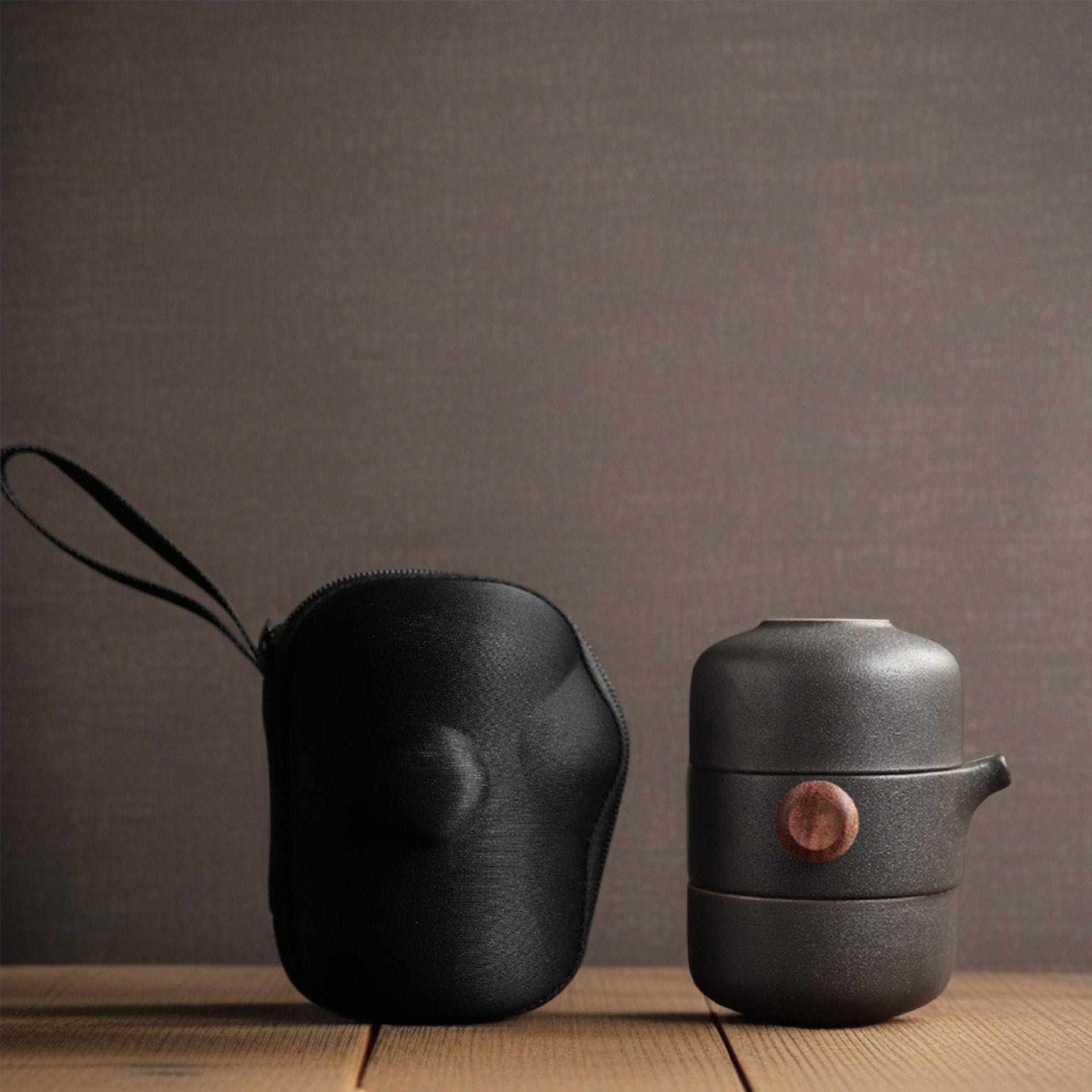  Black ceramic teapot with lid and carrying case on table.
