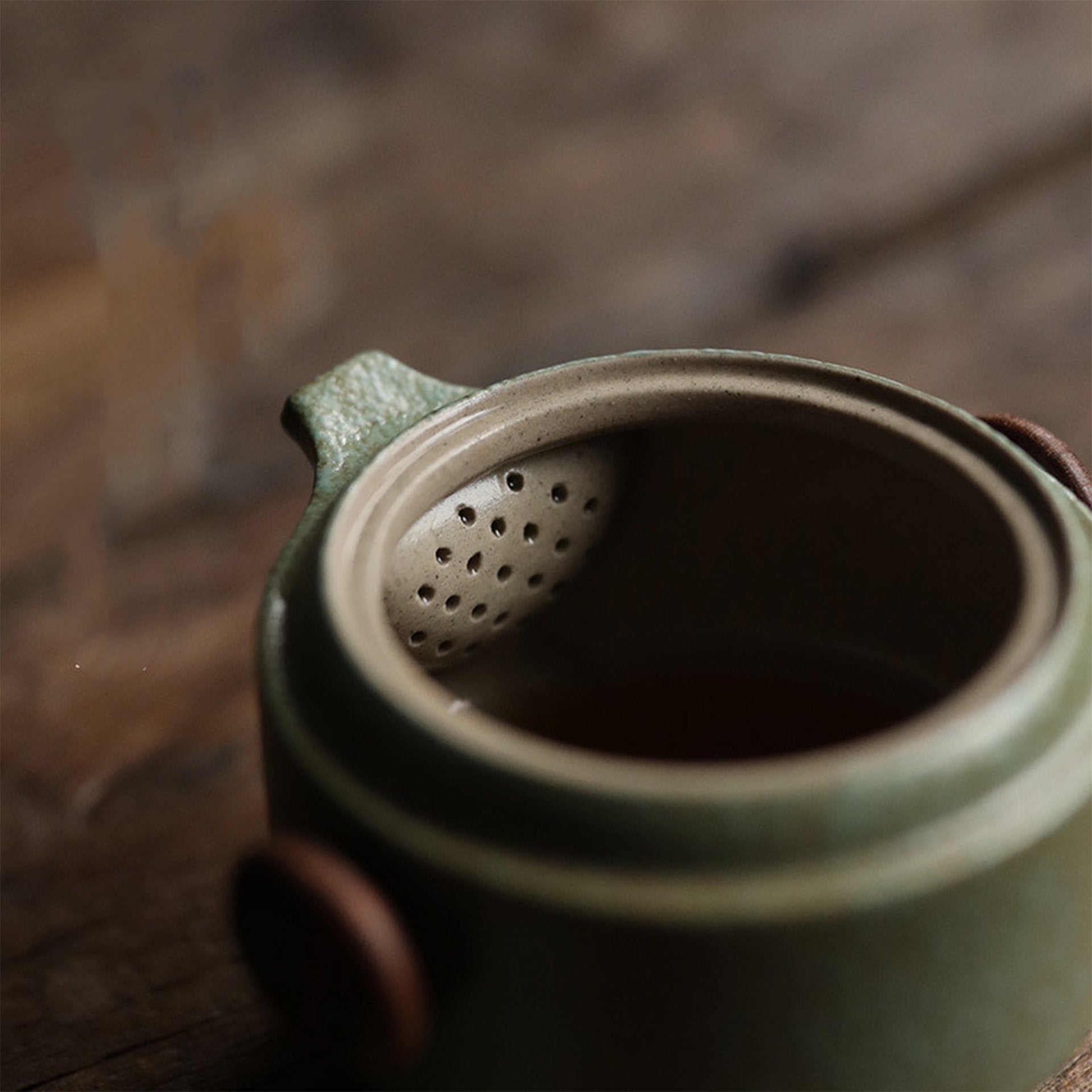 Green ceramic teapot with a strainer lid, partially open, on a wooden table.