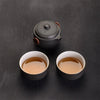 Black teapot with wooden detail and two cups of tea on slate