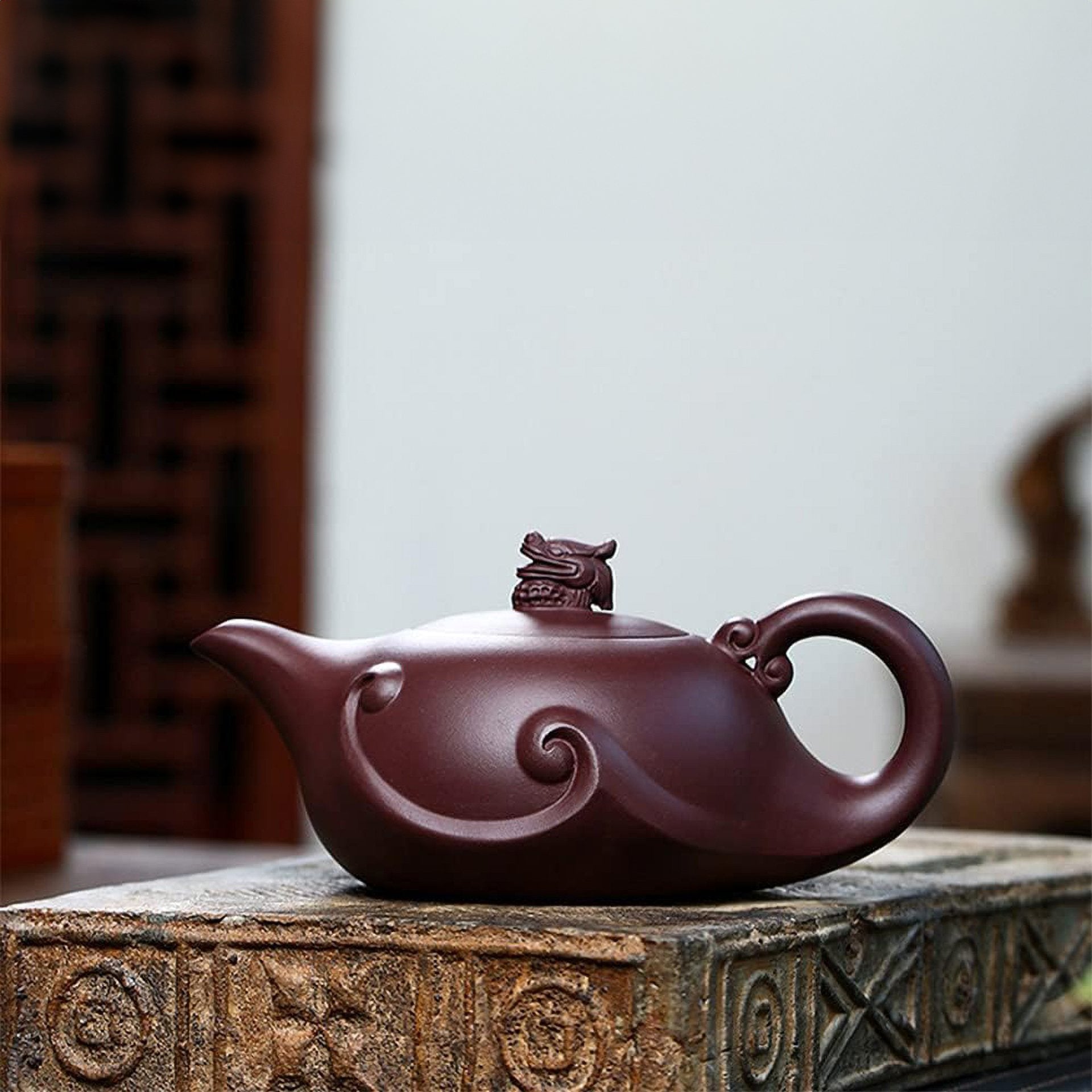 Dark brown teapot with dragon on lid, sitting on an ancient wooden surface.
