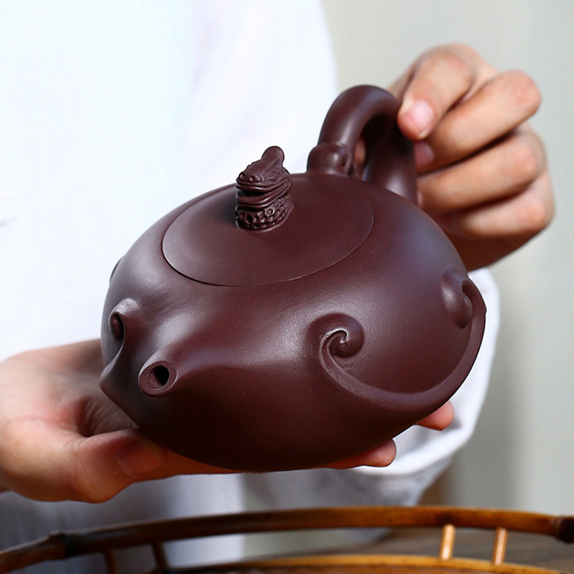 Person holding a large, dark brown teapot with spiral designs.