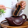 Person pouring tea from a dark brown teapot on a bamboo tray.Person pouring tea from a dark brown teapot on a bamboo tray.
