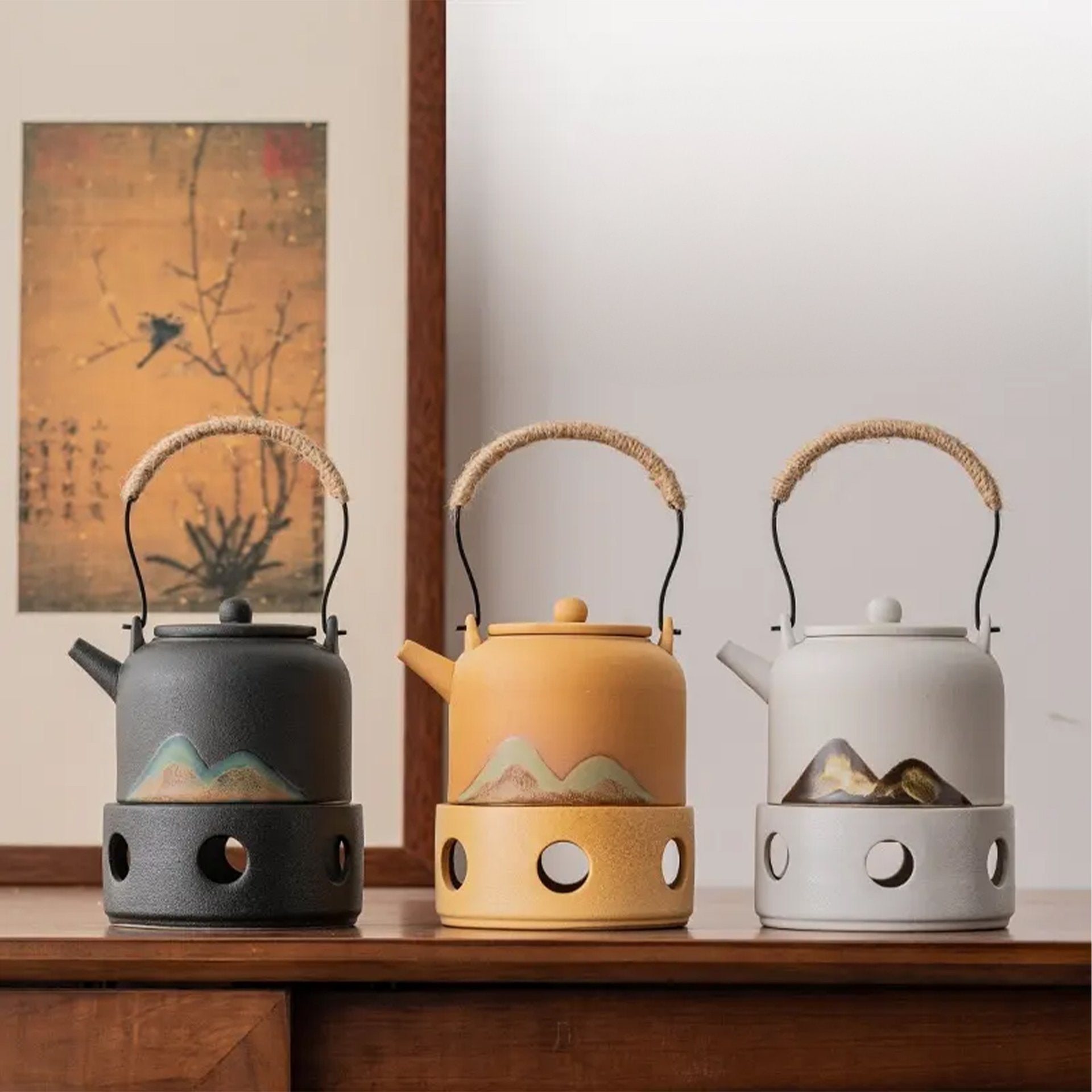 Three ceramic kettles on stoves in front of a painting, displayed on a wooden shelf