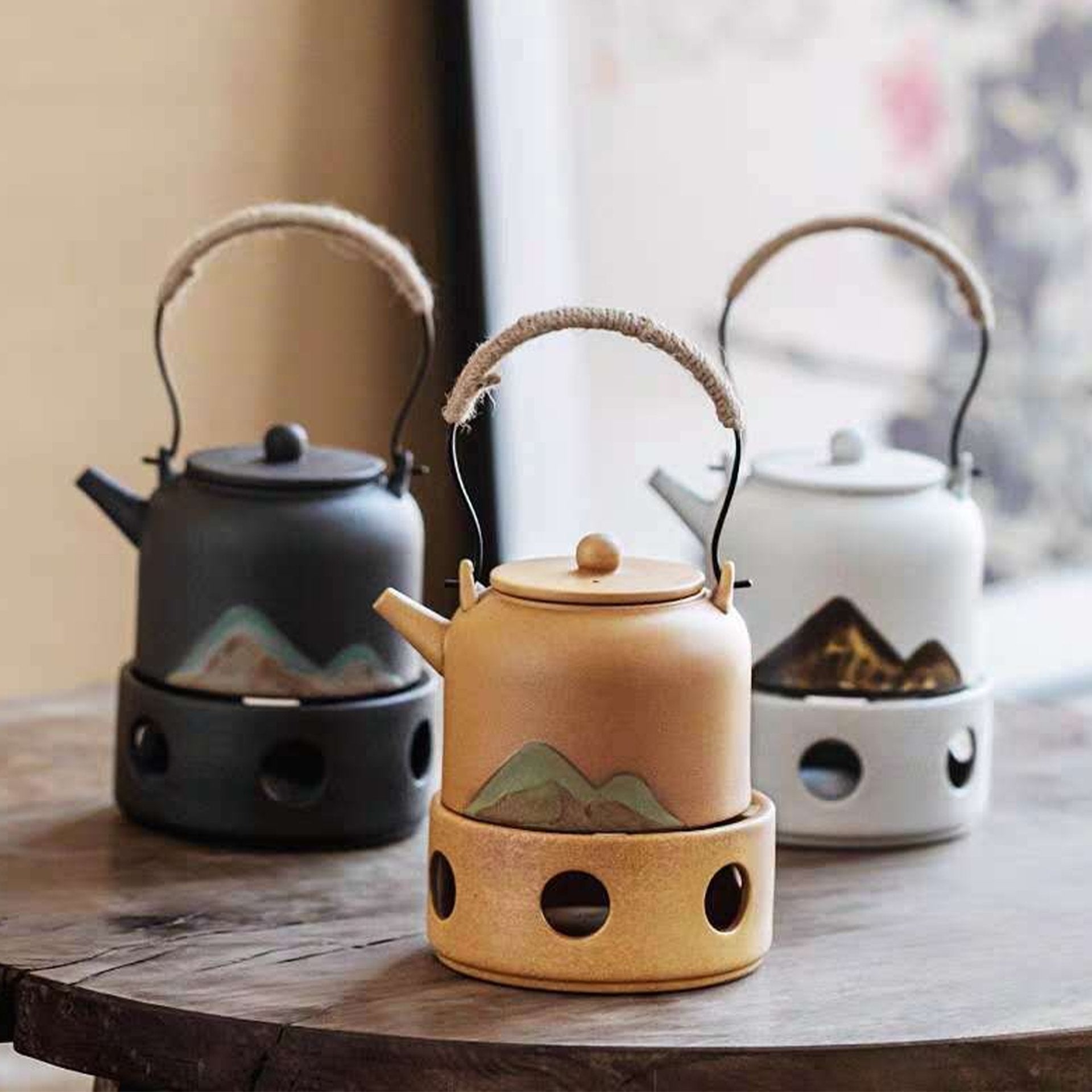 Three ceramic kettles on stoves in black, beige, and white on a wooden surface