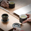 Hands engaging with a black travel tea set and a laptop on a wooden desk.