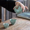 Hand pouring tea from celadon teapot into cup on a wooden table