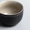 Close-up of a two-toned ceramic bowl with a matte black exterior and glossy beige interior.