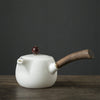 White porcelain teapot with wooden handle and round brown knob on dark grey backdrop.