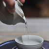 Tea being poured from beige teapot spout into a bowl on saucer